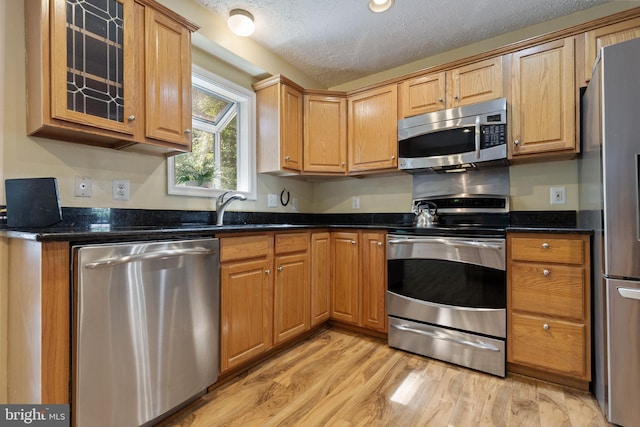 15915 Marlington Dr, Dumfries, VA 22025 - kitchen featuring stainless steel appliances, a textured ceiling, light wood finished floors, glass insert cabinets, and a sink