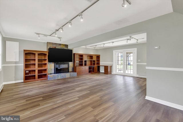 unfurnished living room featuring wood finished floors, baseboards, track lighting, and a stone fireplace