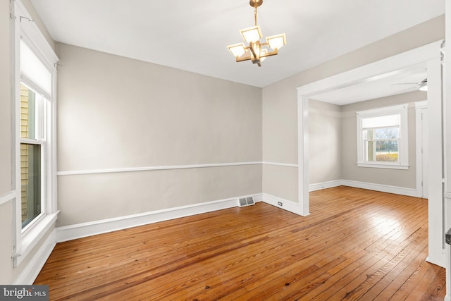 empty room featuring ceiling fan with notable chandelier, baseboards, hardwood / wood-style flooring, and visible vents