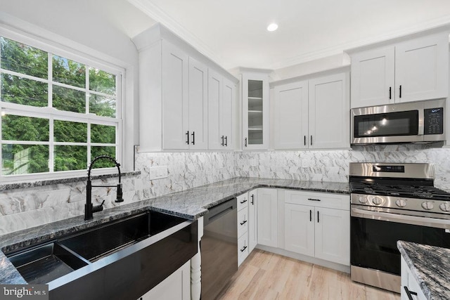 kitchen with stainless steel appliances, a sink, white cabinets, and dark stone counters