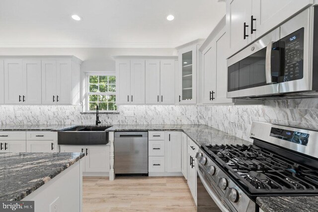 kitchen with stainless steel appliances, a sink, white cabinetry, dark stone countertops, and recessed lighting