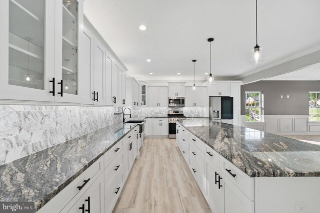 kitchen featuring stainless steel appliances, white cabinetry, a spacious island, tasteful backsplash, and light wood finished floors