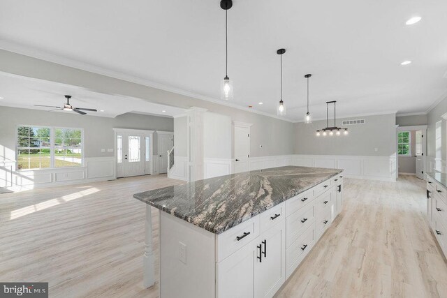 kitchen with a decorative wall, ceiling fan, light wood-style floors, wainscoting, and a center island