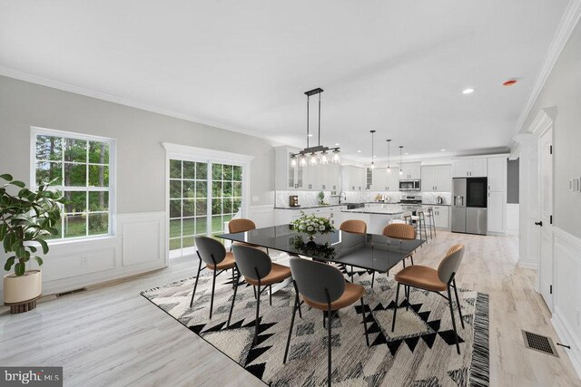 dining space featuring ornamental molding, a wainscoted wall, a decorative wall, and light wood finished floors