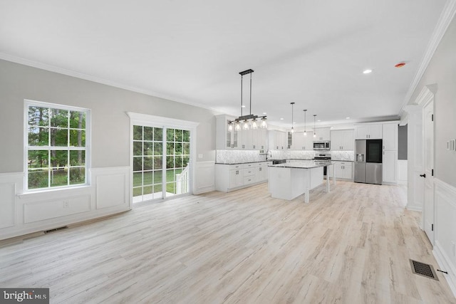 kitchen with stainless steel appliances, white cabinets, a kitchen breakfast bar, ornamental molding, and light wood finished floors