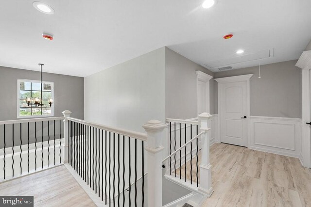 hallway featuring attic access, an upstairs landing, wood finished floors, wainscoting, and a chandelier