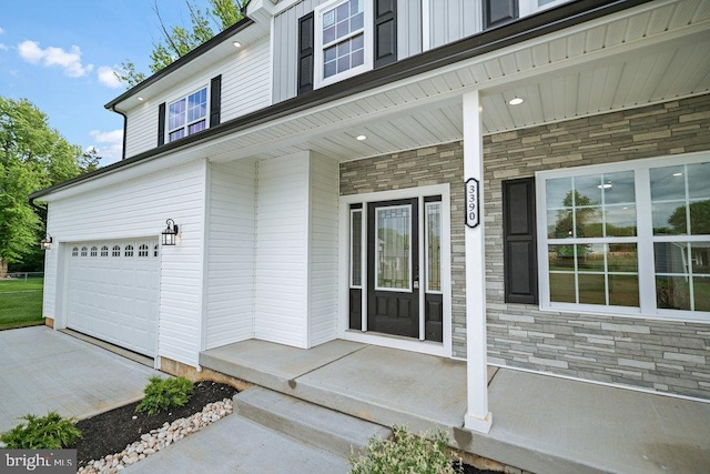property entrance featuring stone siding, a garage, covered porch, and driveway