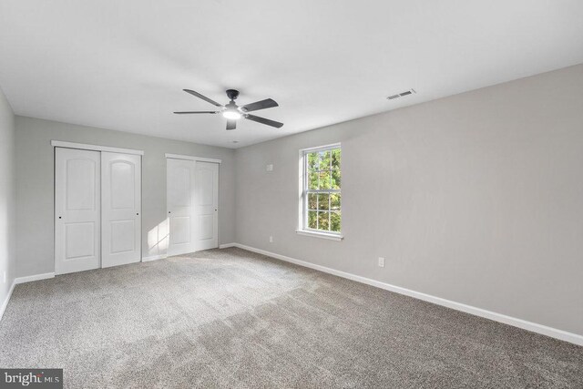 unfurnished bedroom featuring multiple closets, baseboards, carpet, and a ceiling fan