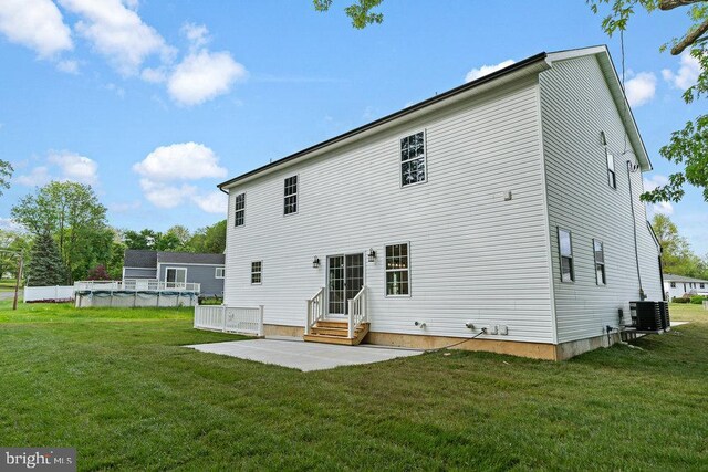 back of house with central AC unit, a patio, an outdoor pool, entry steps, and a lawn