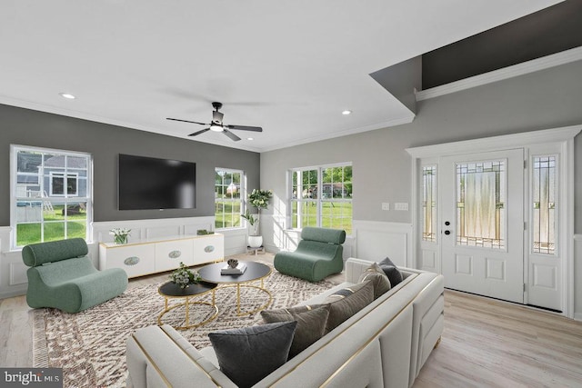 living area with a decorative wall, ornamental molding, a wainscoted wall, ceiling fan, and light wood finished floors