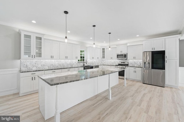 kitchen with stainless steel appliances, white cabinetry, a sink, a kitchen island, and stone counters