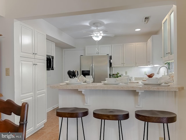 kitchen with a peninsula, a breakfast bar area, stainless steel refrigerator with ice dispenser, white cabinets, and light tile patterned floors