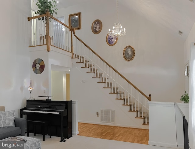 stairway with high vaulted ceiling, visible vents, wood finished floors, and an inviting chandelier
