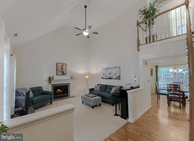 living area with high vaulted ceiling, ceiling fan with notable chandelier, baseboards, wood finished floors, and a tile fireplace
