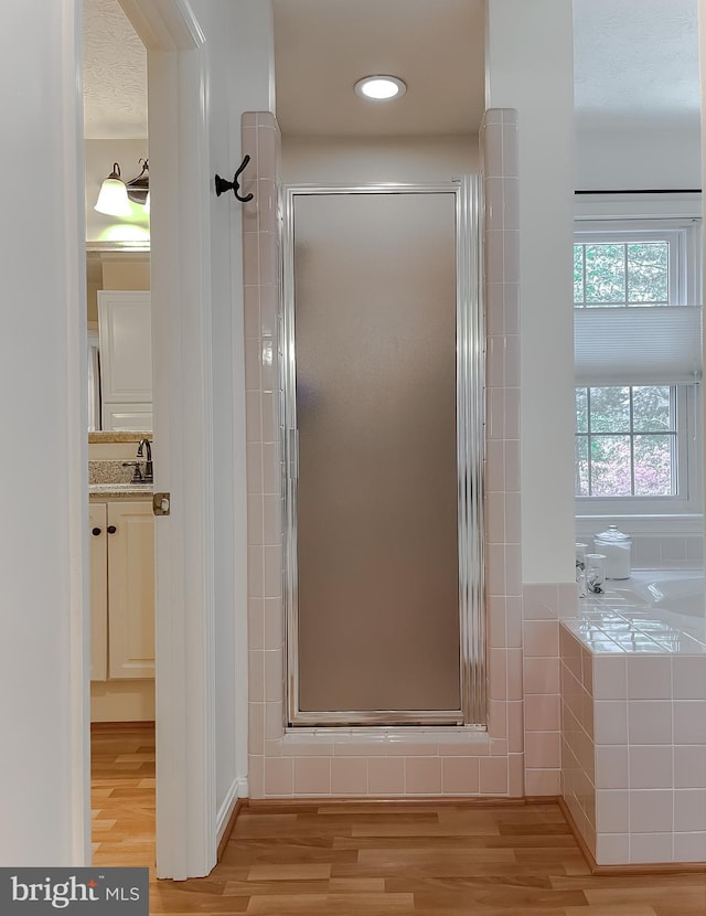 full bath with vanity, a bath, a shower stall, and wood finished floors