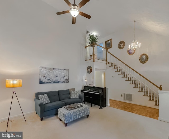 carpeted living room featuring high vaulted ceiling, ceiling fan with notable chandelier, baseboards, visible vents, and stairway
