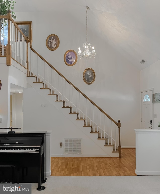 stairs with high vaulted ceiling, a chandelier, wood finished floors, and visible vents