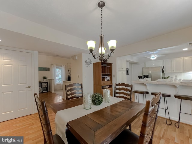 dining space with ceiling fan with notable chandelier and light wood-style flooring