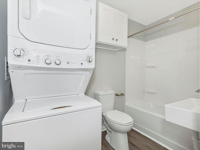 full bathroom with wood finished floors, a sink, washtub / shower combination, toilet, and stacked washer and clothes dryer