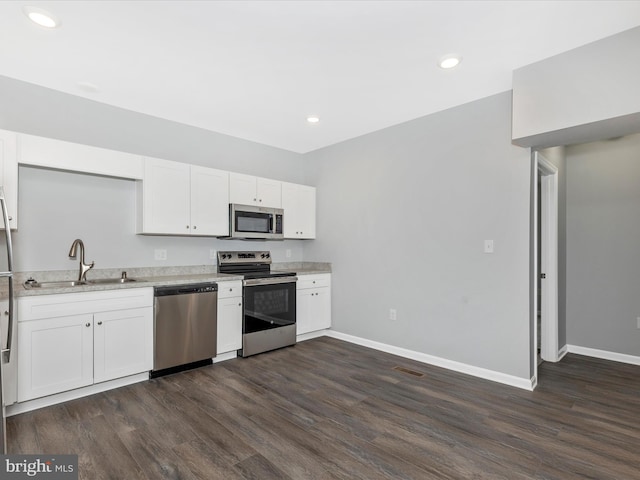 kitchen with a sink, stainless steel appliances, white cabinets, baseboards, and dark wood-style floors