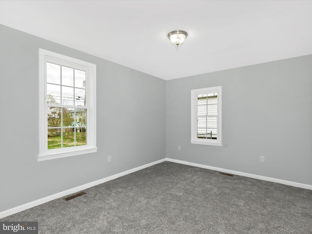 unfurnished room featuring baseboards, dark colored carpet, and visible vents