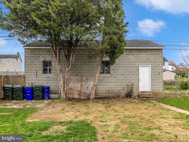 back of house featuring fence, concrete block siding, a shingled roof, and entry steps