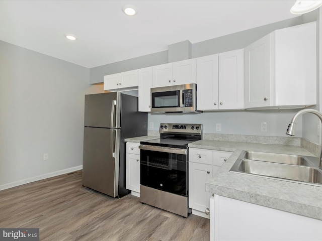 kitchen featuring white cabinets, light countertops, a sink, light wood-style floors, and appliances with stainless steel finishes