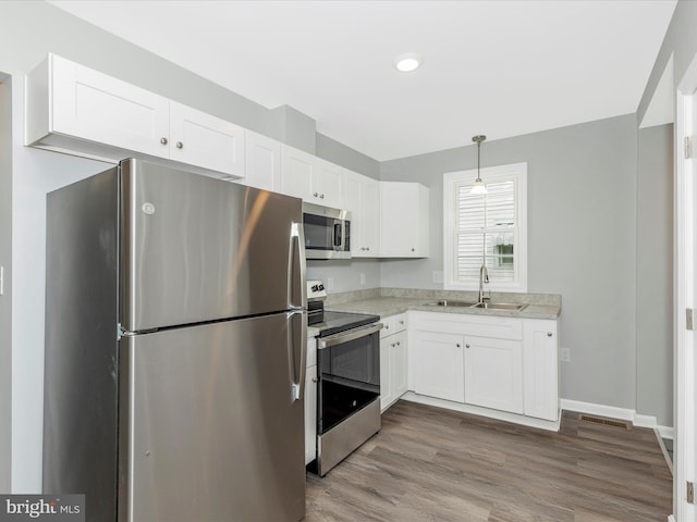 kitchen featuring wood finished floors, a sink, white cabinets, appliances with stainless steel finishes, and visible vents