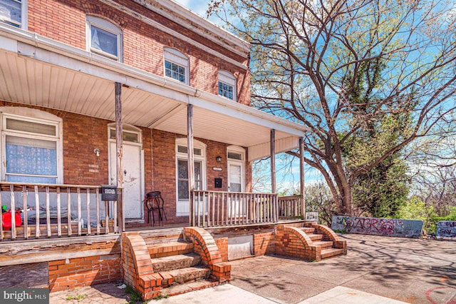 view of exterior entry featuring covered porch and brick siding