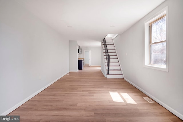 hall with stairway, baseboards, light wood-type flooring, and visible vents