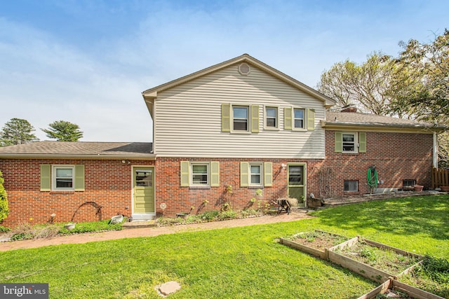 back of house featuring a chimney, a garden, brick siding, a shingled roof, and a lawn