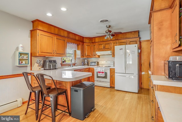 kitchen featuring a sink, a baseboard radiator, under cabinet range hood, white appliances, and a peninsula