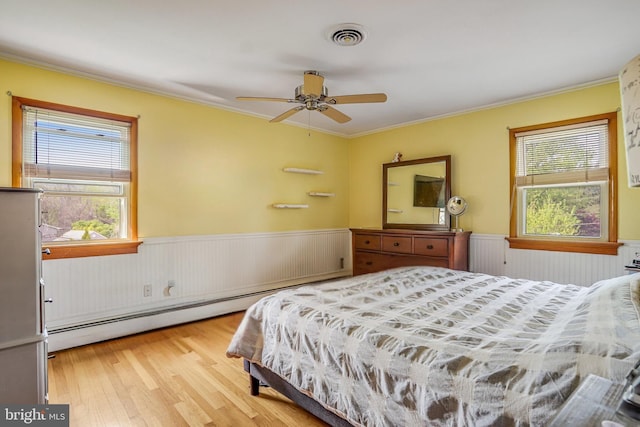 bedroom featuring light wood-style flooring, wainscoting, baseboard heating, visible vents, and crown molding
