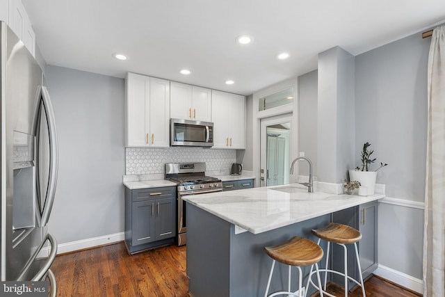 kitchen with appliances with stainless steel finishes, a sink, light stone counters, a breakfast bar, and recessed lighting