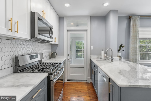 kitchen with appliances with stainless steel finishes, a sink, gray cabinets, light stone counters, and dark wood finished floors