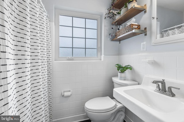 bathroom featuring a sink, toilet, tile walls, wainscoting, and a shower with shower curtain