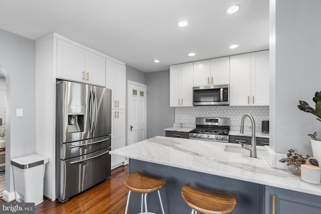 kitchen with stainless steel appliances, arched walkways, a kitchen bar, light stone countertops, and recessed lighting