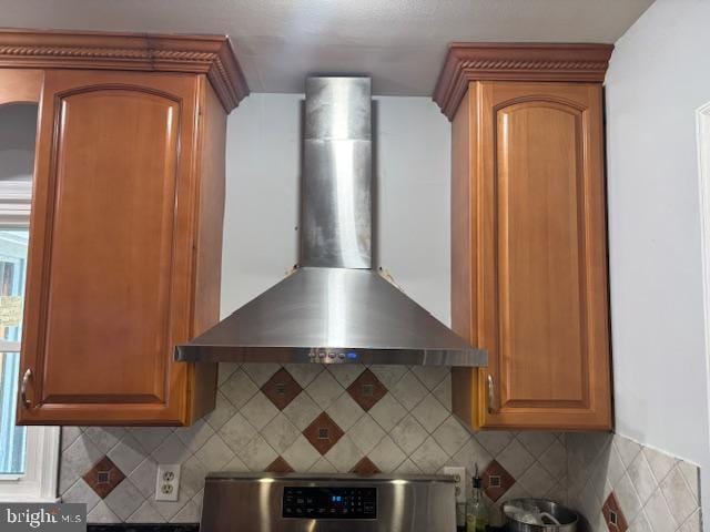 kitchen with wall chimney range hood, backsplash, range, and brown cabinets