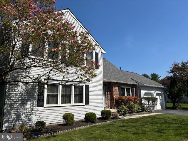 view of front facade with a front yard, a shingled roof, aphalt driveway, and an attached garage
