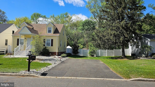 cape cod home with fence, a front lawn, and aphalt driveway