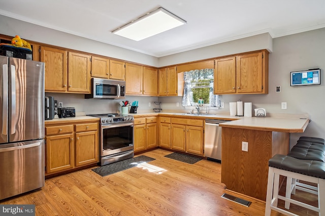 813 Petinot Pl, Stevensville, MD 21666 - kitchen with stainless steel appliances, a peninsula, a sink, light wood-style flooring, and ornamental molding