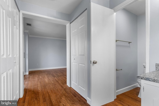 hall with baseboards, crown molding, wood finished floors, and visible vents