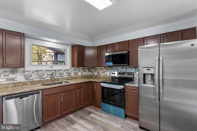 kitchen featuring a sink, tasteful backsplash, light wood-type flooring, light stone counters, and appliances with stainless steel finishes