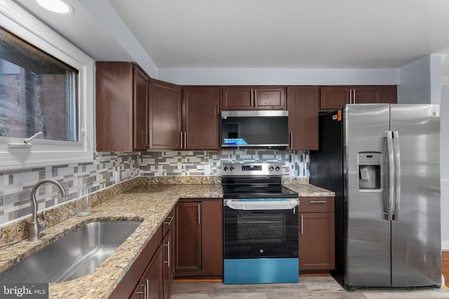 kitchen with a sink, tasteful backsplash, light wood-style floors, light stone counters, and appliances with stainless steel finishes