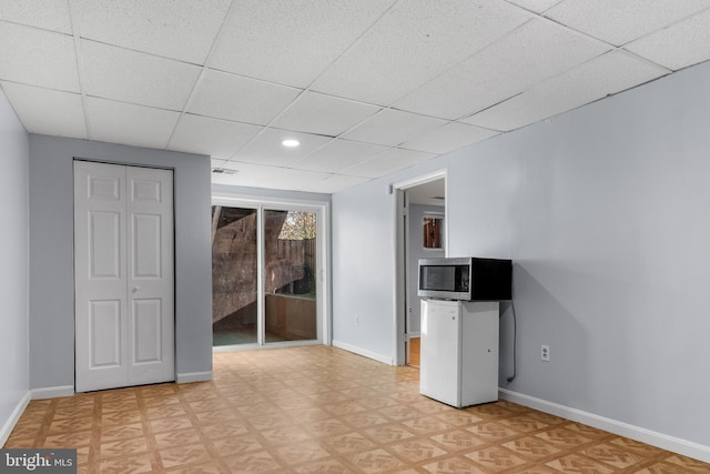 unfurnished living room featuring light floors, baseboards, a drop ceiling, and recessed lighting