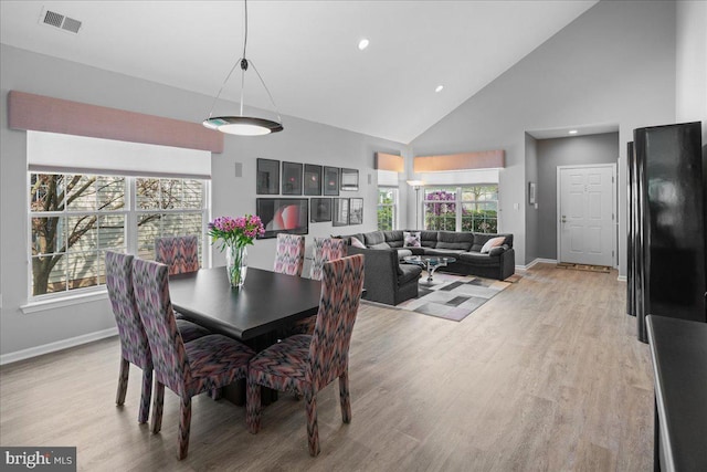 dining space with visible vents, light wood-style flooring, high vaulted ceiling, and baseboards