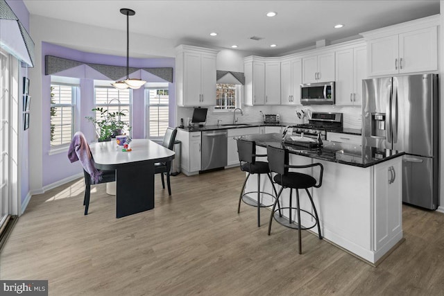 kitchen featuring decorative backsplash, a breakfast bar, stainless steel appliances, white cabinetry, and light wood-type flooring