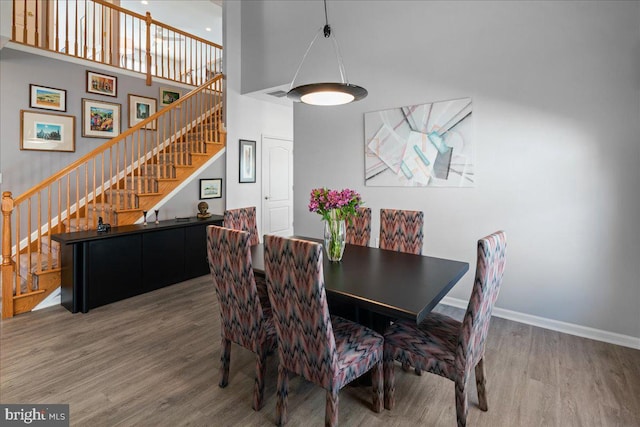 dining room featuring a high ceiling, baseboards, wood finished floors, and stairs