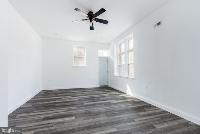 empty room with plenty of natural light, a ceiling fan, visible vents, and dark wood-style flooring