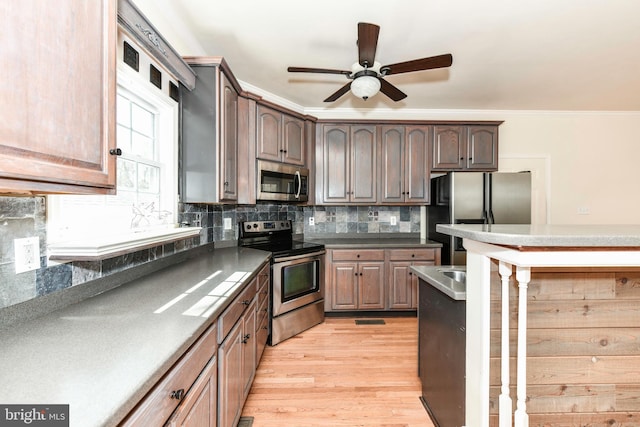 kitchen with a kitchen breakfast bar, tasteful backsplash, light wood-style floors, ceiling fan, and appliances with stainless steel finishes